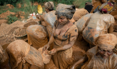 Des femmes portant des sacs en plastique par-dessus leurs vêtements  pour se protéger de la boue lavent des roches dans l’eau à la recherche de particules d’or sur un site minier artisanal à Mongbwalu, dans la province de l’Ituri, en RDCongo, le 16 juin 2026. ( AFP / Jospin Mwisha )