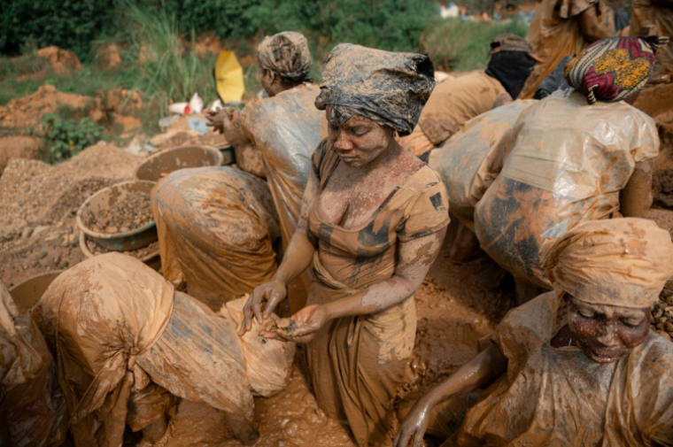 Des femmes portant des sacs en plastique par-dessus leurs vêtements  pour se protéger de la boue lavent des roches dans l’eau à la recherche de particules d’or sur un site minier artisanal à Mongbwalu, dans la province de l’Ituri, en RDCongo, le 16 juin 2026. ( AFP / Jospin Mwisha )