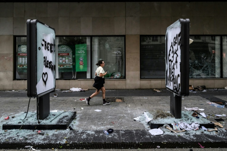 Une joggeuse passe devant des vitrines de commerces brisées et des panneaux tagués et endommages, au lendemain d'une manifestation contre la vie chère à Lyon, le 18 octobre 2026 ( AFP / JEFF PACHOUD )