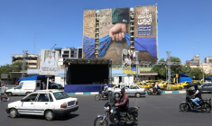 Des véhicules devant un panneau d'affichage sur la façade d'un bâtiment représentant le détroit d'Ormuz avec une légende en persan disant "À jamais dans la main de l'Iran", place Vanak à Téhéran, le 25 mai 2026 ( AFP / ATTA KENARE )