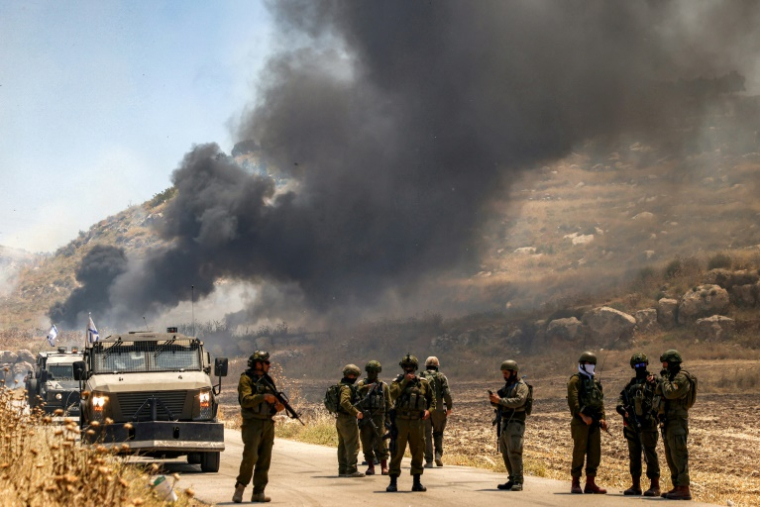 Des forces de sécurité israéliennes montent la garde le long d'une route tandis que de la fumée s'élève d'une zone qui aurait été incendiée par des colons israéliens dans le village palestinien d'Idna, à l'ouest d'Hébron, en Cisjordanie occupée, le 5 juin 2026 ( AFP / HAZEM BADER )