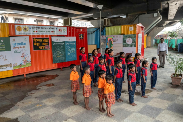 Des élèves chantent l'hymne national indien à "l'école du feu rouge" qui accueille des enfants défavorisés dans des conteneurs aménagés en salles de cours sous un pont autoroutier, le 18 mai 2026 à Bombay ( AFP / Punit PARANJPE )