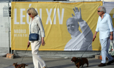 Deux personnes promènent leur chien près d'une affiche annonçant la venue du pape Léon XIV, le 5 juin 2026 à Madrid ( AFP / Thomas COEX )