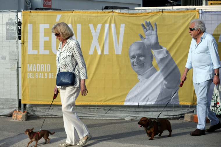 Deux personnes promènent leur chien près d'une affiche annonçant la venue du pape Léon XIV, le 5 juin 2026 à Madrid ( AFP / Thomas COEX )