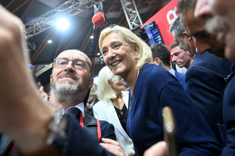 La cheffe de file du Rassemblement nationale, Marine Le Pen, fait un selfie avec un exposant lors du congrès des sapeurs-pompiers au Mans, le 10 octobre 2025 dans la Sarthe ( AFP / JEAN-FRANCOIS MONIER )