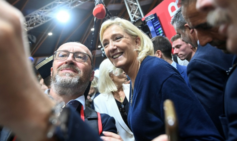 La cheffe de file du Rassemblement nationale, Marine Le Pen, fait un selfie avec un exposant lors du congrès des sapeurs-pompiers au Mans, le 10 octobre 2025 dans la Sarthe ( AFP / JEAN-FRANCOIS MONIER )