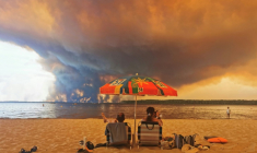 Des personnes sur la plage du Moutchic à Lacanau, dans le sud-ouest de la France, le 24 juillet 2026, tandis que des nuages de fumée d'un incendie s’élèvent dans le ciel  ( AFP / Maximilien LAMY )