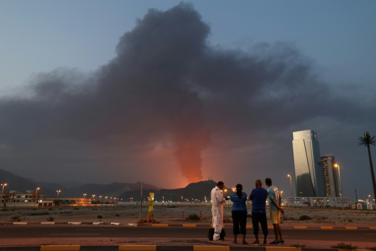 Des travailleurs étrangers observent un panache de fumée noire après une explosion dans la zone industrielle de Fujairah, le 3 mars 2026 aux Emirats arabes unis ( AFP / Fadel SENNA )