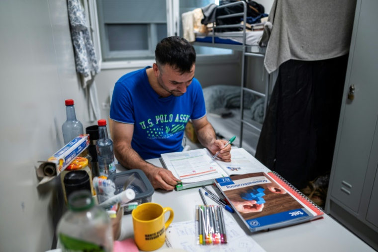 Kurde de Turquie, Faruk Polat, révise ses cours d'allemand dans un camp pour réfugiés dans des hangars de l'ancien aéroport berlinois de Tempelhof , le 14 août 2025 ( AFP / John MACDOUGALL )