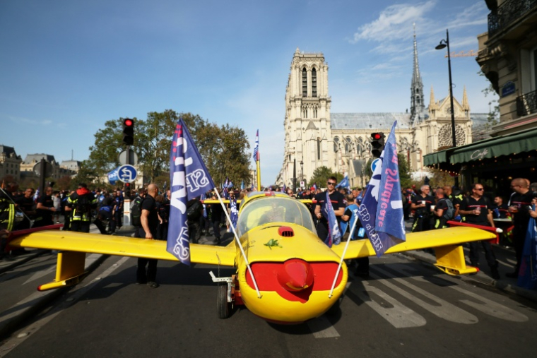 Des pompiers installent un avion peint aux couleurs de la Sécurité civile devant la cathédrale Notre-Dame de Paris, lors d'une manifestation pour réclamer des hausses de salaires et des moyens budgétaires accrus, le 28 septembre 2026 à Paris ( AFP / Xavier GALIANA )