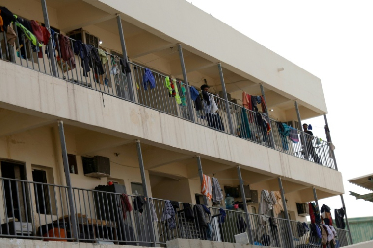 Des travailleurs étrangers sur le balcon de leurs logements observent un panache de fumée après une frappe iranienne présumée dans le quartier industriel de Doha, le 1er mars 2026 au Qatarcorrespondents and residents heard fresh explosions across the Gulf cities of Dubai, Abu Dhabi, Doha and Manama on March 1, as Iran pressed on with its retaliatory campaign for a second day. ( AFP / - )