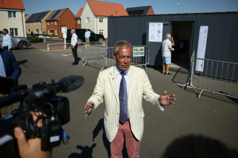 Nigel Farage, (c) chef du parti britannique Reform UK, fait une déclaration aux médias à la sortie d'un bureau de vote installé dans une école primaire de Walton-on-the-Naze, dans l'Essex, lors de l'élection partielle de Clacton, le 13 août 2026 ( AFP / Henry NICHOLLS )