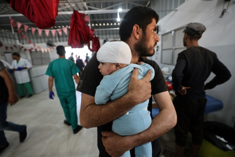Un Palestinien tient dans ses bras un enfant blessé après avoir reçu des soins à l'hôpital Al-Awda à Nousseirat, dans le centre de la bande de Gaza, le 19 mai 2025 ( AFP / Eyad BABA )