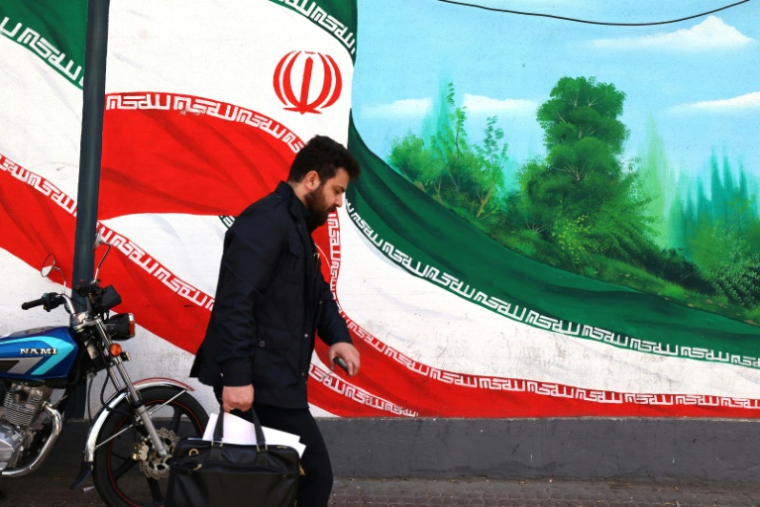 Une Iranien marche près d'une fresque représentant le drapeau national, à Téhéran le 22 février 2026 ( AFP / ATTA KENARE )