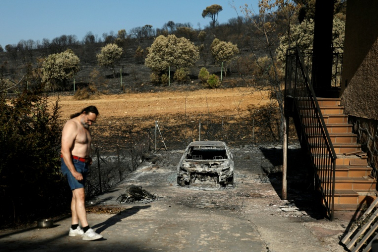 Un homme se tient à côté de sa voiture calcinée sur sa propriété, dévastée par un incendie de forêt dans le lotissement d'Encinar del Alberche, à Villa del Prado, au sud-ouest de Madrid, en Espagne, le 30 juillet 2026 ( AFP / Oscar DEL POZO )