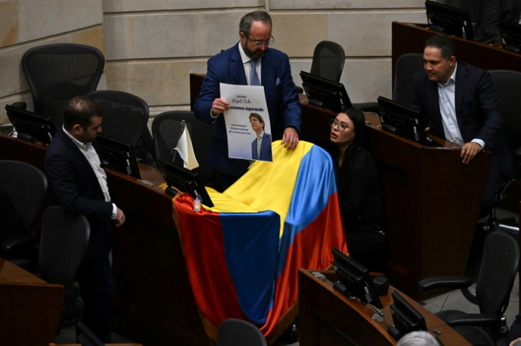Des membres du Sénat colombien déposent une photo de Miguel Uribe avec la phrase "Nous t'attendons" sur un drapeau colombien au-dessus de son siège au Parlement à Bogota, le 9 juin 2025 ( AFP / Raul ARBOLEDA )