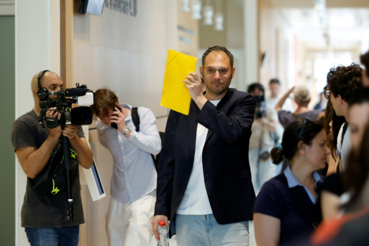 David G., animateur périscolaire, se cache le visage avec un dossier à son arrivée au tribunal où il doit être jugé pour agressions sexuelles sur neuf enfants, le 26 mai 2026 ( AFP / SIMON WOHLFAHRT )