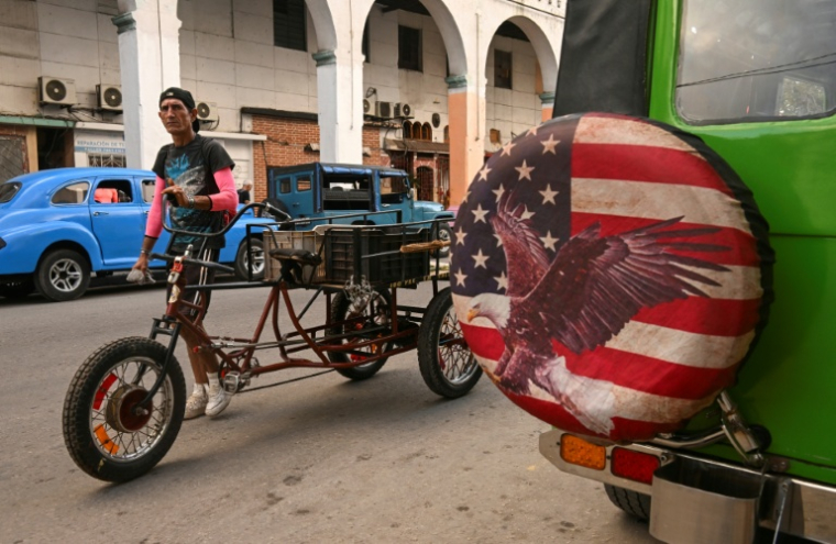 Un homme pousse un vélo devant une jeep arborant une housse de roue ornée d’une image inspirée du drapeau américain, à La Havane, la capitale cubaine, le 23 janvier 2026. ( AFP / YAMIL LAGE )