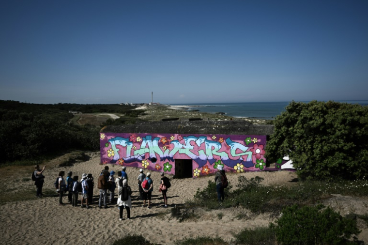 Des touristes devant les vestiges d'un blockhaus de la Seconde Guerre mondiale désormais recouvert de graffitis, sur la côte atlantique à Soulac-sur-Mer, en Gironde, le 15 mai 2025 ( AFP / Philippe LOPEZ )