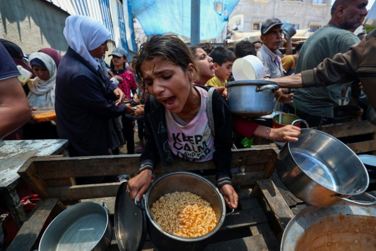 Une fillette reçoit de la nourriture tandis que d'autres Palestiniens attendent à un point de distribution de repas à Nousseirat, dans le centre de la bande de Gaza, le 2 juin 2025 ( AFP / Eyad BABA )