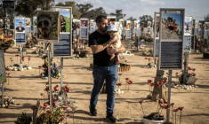 Un homme portant un bébé passe devant les photos des victimes de l'attaque du Hamas le 7 octobre 2023, au mémorial du massacre du festival Nova, à Réïm dans le sud d'Israël, le 6 octobre 2025 ( AFP / JOHN WESSELS )