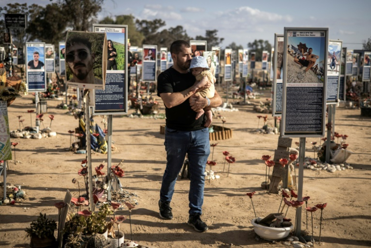 Un homme portant un bébé passe devant les photos des victimes de l'attaque du Hamas le 7 octobre 2023, au mémorial du massacre du festival Nova, à Réïm dans le sud d'Israël, le 6 octobre 2025 ( AFP / JOHN WESSELS )