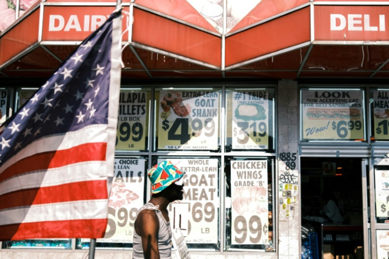 Une personne passe devant une épicerie et un drapeau américain dans le quartier de Flatbush, surnommé "Little Haiti", dans l'arrondissement de Brooklyn à New York, aux Etats-Unis, le 15 juillet 2025 ( AFP / CHARLY TRIBALLEAU )