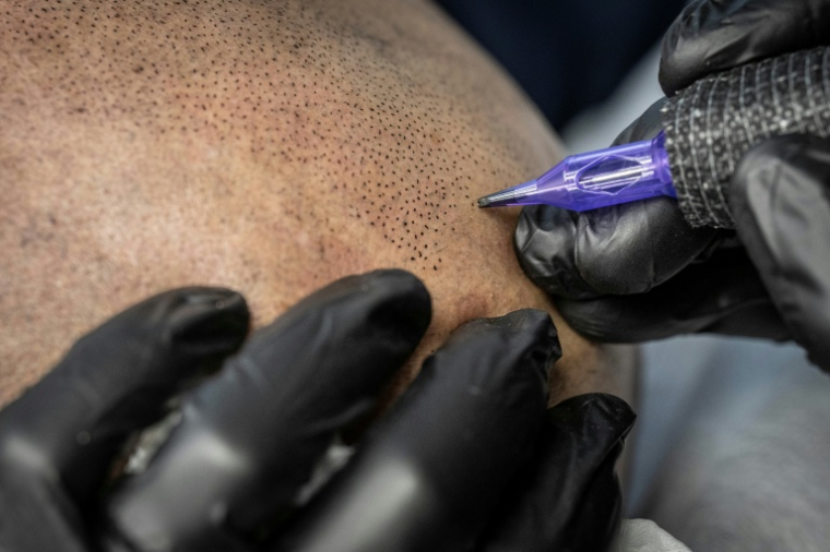 Remy, tatoueur professionnel, réalise une intervention de micropigmentation du cuir chevelu sur un client, dans son studio de Ginowan, à Okinawa au Japon, le 19 mai 2026 ( AFP / Yuichi YAMAZAKI )