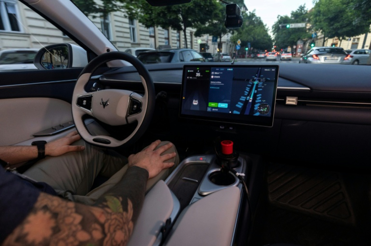 Le volant et l'écran de contrôle d'un robotaxi Verne à Zagreb, en Croatie, avec un opérateur de sécurité mains sur les genoux, le 4 mai 2026 ( AFP / MARKO PERKOV )