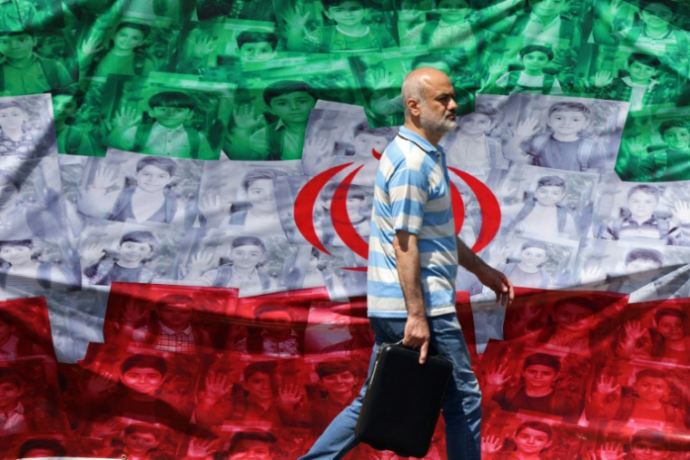 Un homme passe devant un drapeau iranien installé le long de la route à Téhéran le 29 avril 2026 ( AFP / ATTA KENARE )