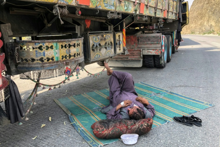Un chauffeur de camion se repose à côté de son véhicule en panne près de la ville frontalière de Torkham entre le Pakistan et l'Afghanistan, le 19 octobre 2025 ( AFP / Basit GILANI )