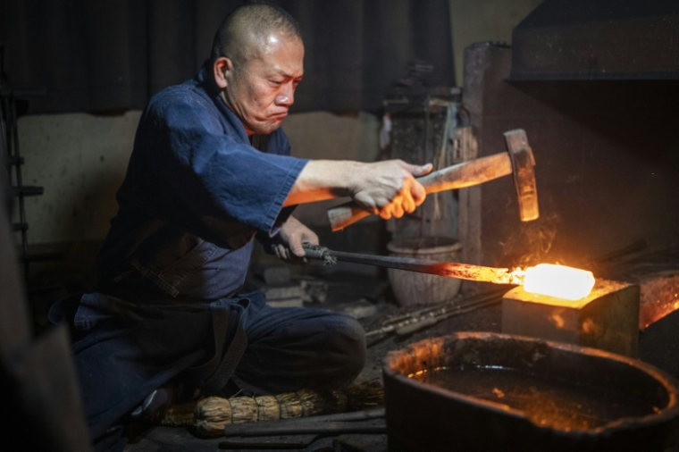 Le forgeron Akihira Kawasaki martèler de l'acier pour forger une lame de katana dans son atelier à Misato, le 9 janvier 2026 au Japon ( AFP / Yuichi YAMAZAKI )