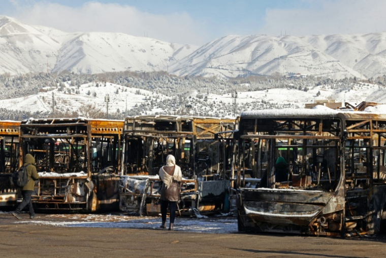 Des journalistes regardent des bus incendiés à Téhéran durant des manifestations récentes, lors d'une visite organisée par les autorités iraniennes pour la presse étrangère, le 21 janvier 2026 ( AFP / ATTA KENARE )