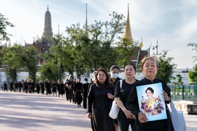 Des personnes en deuil tiennent des portraits de l'ancienne reine Sirikit de Thaïlande en faisant la queue pour rendre hommage à la défunte reine au Grand Palais de Bangkok, le 26 octobre 2025 ( AFP / Chanakarn Laosarakham )
