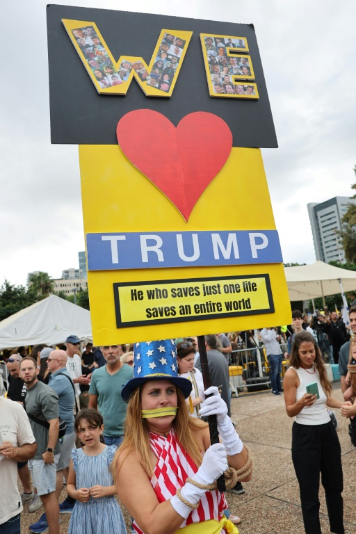 Une femme vêtue aux couleurs du drapeau américain brandit une pancarte disant "we love Trump" le 9 octobre sur la place des otages à Tel-Aviv, où des milliers de personnes se sont rassemblées pour fêter l'accord conclu entre Israël et le Hamas ( AFP / Jack GUEZ )