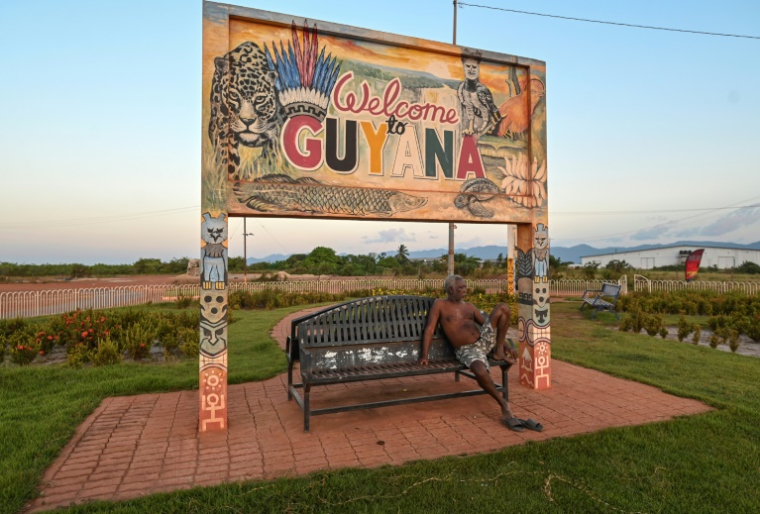 Un homme assis sur un banc sous un panneau à la frontière entre le Guyana et le Brésil, le 27 août 2025 près de Lethem, dans le sud-ouest du Guyana ( AFP / Joaquin Sarmiento )
