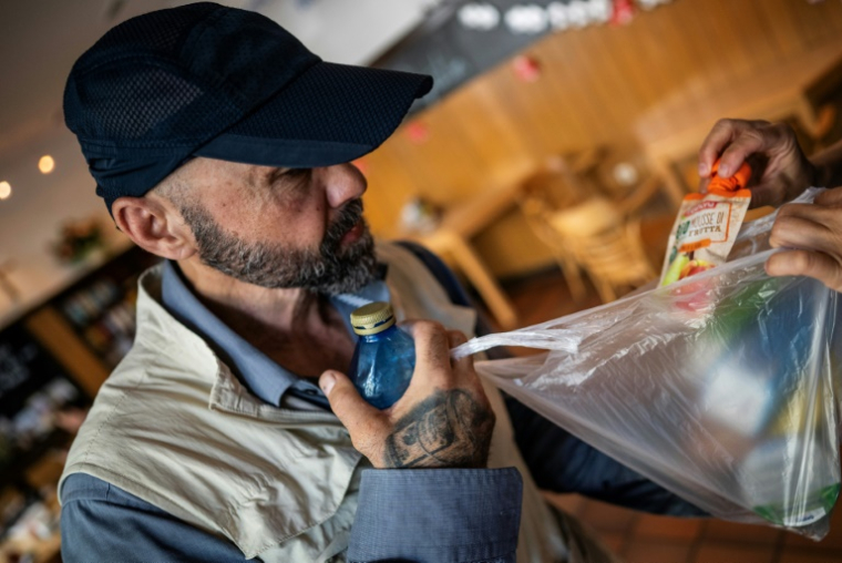 Une personne sans-abri découvre le contenu d'un "kit canicule", composé de denrées alimentaires, d'eau, d'autres liquides et de crème solaire, dans un centre communautaire à Berlin, le 25 juin 2026 ( AFP / John MACDOUGALL )