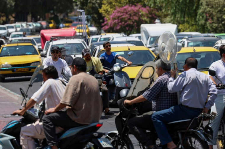 Un homme tient un ventilateur alors qu'il se déplace à moto dans une rue de Téhéran, pendant une vague de chaleur en Iran, le 22 juillet 2025 ( AFP / - )