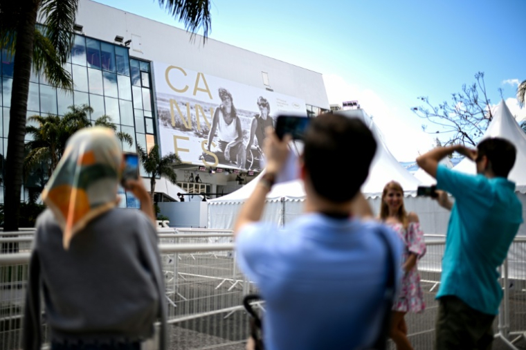 Des passants photographient la façade du Palais du festival à Cannes le 11 mai 2026 ( AFP / Anna KURTH )