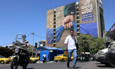 Des passants traversent une rue devant un panneau d'affichage apposé sur la façade d'un immeuble représentant le détroit d'Ormuz, avec une légende en persan indiquant "Pour toujours entre les mains de l'Iran", à Téhéran, le 25 mai 2026 ( AFP / ATTA KENARE )