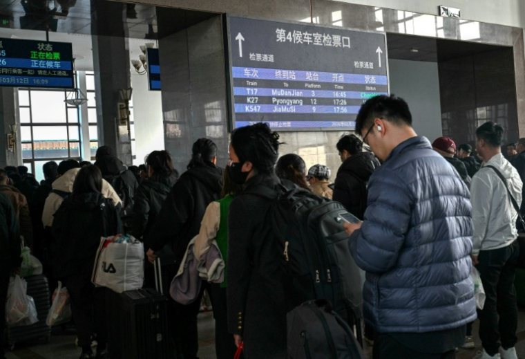 Des voyageurs font la queue à côté d'un panneau indiquant le train K27 à destination de Pyongyang, à la gare de Pékin, le 12 mars 2026 en Chine ( AFP / ADEK BERRY )