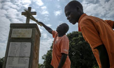 Wilfred Lalobo (centre), 60 ans, un survivant du massacre de Lukodi le 19 mai 2004, et Richard Ochola, 34 ans, un employé du mémorial de Lukodi, nettoie une stèle commémorative du massacre perpétré il a plus de 20 ans pzr la guérilla de la LRA dans ce village du nord de l'Ouganda, le 4 septembre 2025. ( AFP / Stuart Tibaweswa )