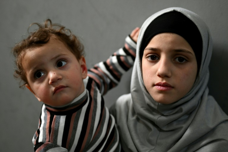 Une jeune fille porte son frère dans un couloir d’une école transformée en centre d’accueil pour personnes déplacées, dans la région de Dekwaneh, à l’est de Beyrouth, le 15 avril 2026 ( AFP / Joseph EID )