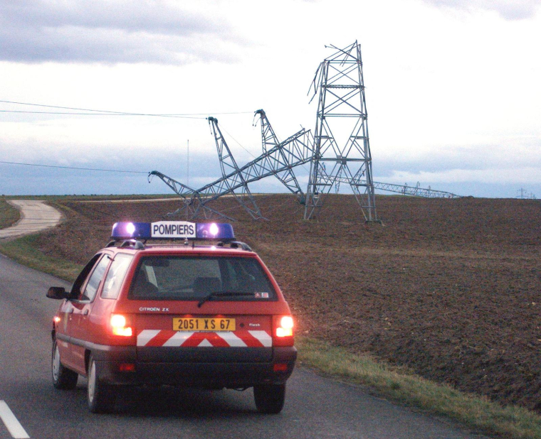 une voiture des sapeurs pompiers de Truchtersheim passe ,le 26 décembre 1999, devant les pylônes d'une ligne haute tension de 20 000 volts abattus par le vent ( AFP / DAMIEN MEYER )