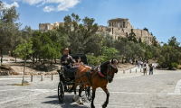 Des touristes en calèche passent devant la colline de l'Acropole, le 29 mai 2025 à Athènes ( AFP / Aris MESSINIS )