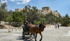 Des touristes en calèche passent devant la colline de l'Acropole, le 29 mai 2025 à Athènes ( AFP / Aris MESSINIS )