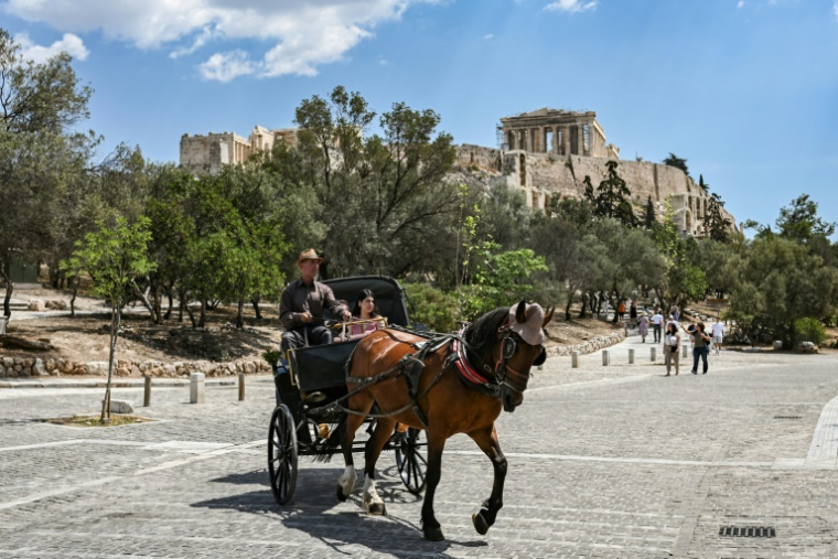 Des touristes en calèche passent devant la colline de l'Acropole, le 29 mai 2025 à Athènes ( AFP / Aris MESSINIS )
