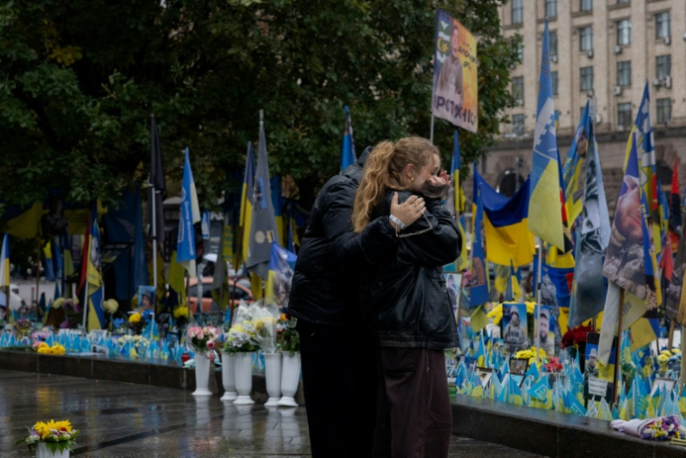 Des passants devant un mémorial improvisé pour les soldats ukrainiens et étrangers morts au combat, le 7 octobre 2025 à Kiev  ( AFP / Tetiana DZHAFAROVA )