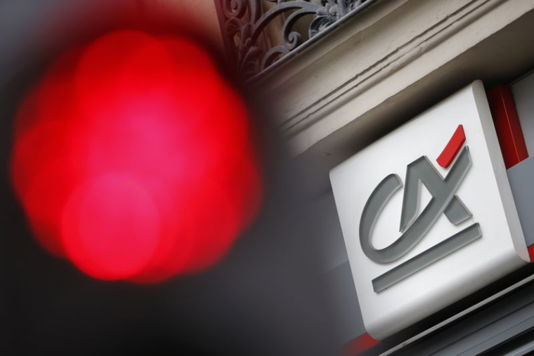 Un feu de signalisation est allumé au rouge près du logo du Crédit Agricole, visible sur une agence bancaire à Paris