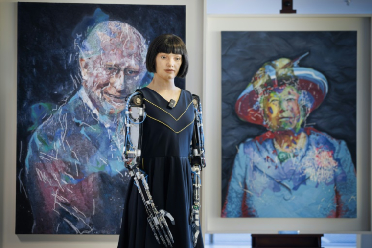 Le robot artiste gynoïde Ai-Da devant les portraits du roi Charles III et de la reine Elizabeth II d'Angleterre qu'il a peints, exposés en marge du Sommet mondial AI for Good organisé par l'Union internationale des télécommunications (UIT) à Genève, le 9 juillet 2025 ( AFP / Valentin Flauraud )